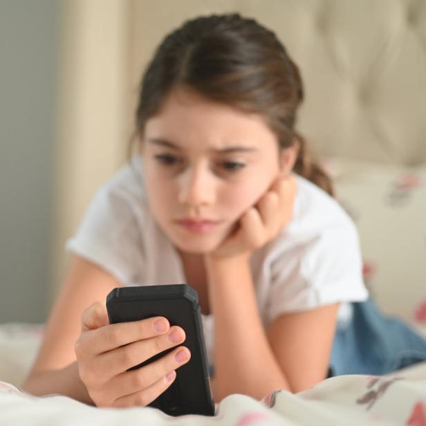 Ein Kind liegt mit einem Smartphone auf dem Bett.