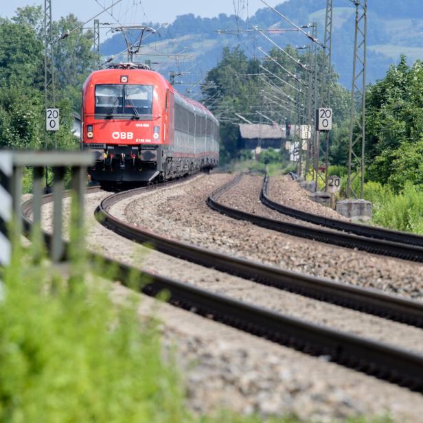 Ein roter ÖBB-Zug fährt auf einer kurvenreichen Strecke durch eine grüne Landschaft.