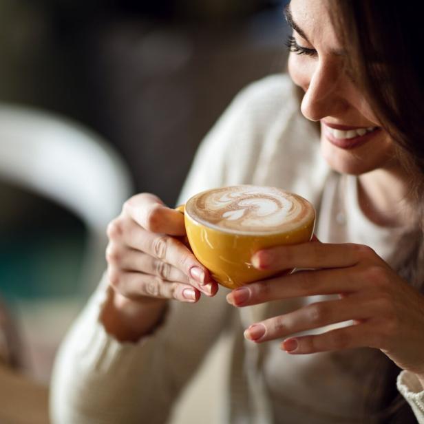 Eine Frau hält eine Tasse Kaffee und lächelt.