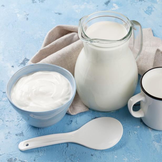 Ein Krug Milch, eine Schüssel Joghurt und eine Tasse Milch auf blauem Grund.
