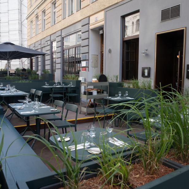 Das Restaurant „O boufés“ mit Tischen im Freien und viel Grün im Außenbereich.