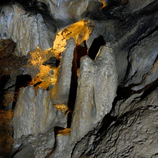Verschiedene Stalagmiten ragen in einer dunklen Höhle empor.