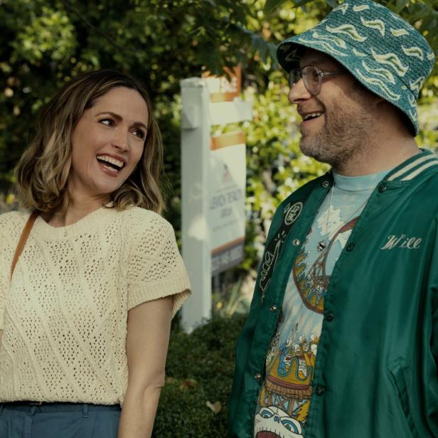 Rose Byrne und Seth Rogen stehen lachend vor einem „Zu verkaufen“-Schild.