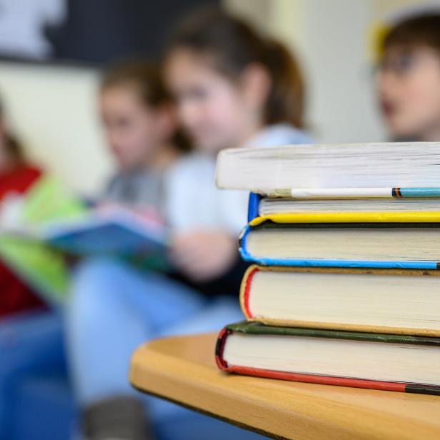 Ein Stapel Bücher liegt vor lesenden Schülern und Schülerinnen einer Volksschule.