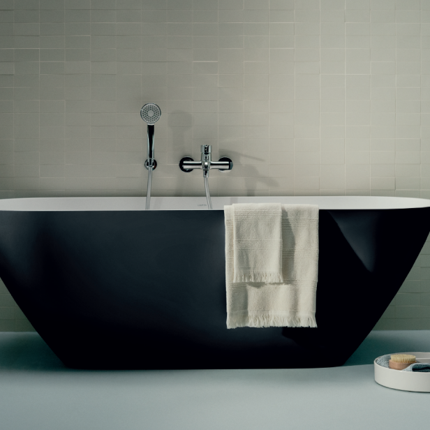 Eine freistehende, schwarze Badewanne mit einem weißen Handtuch und Badutensilien.