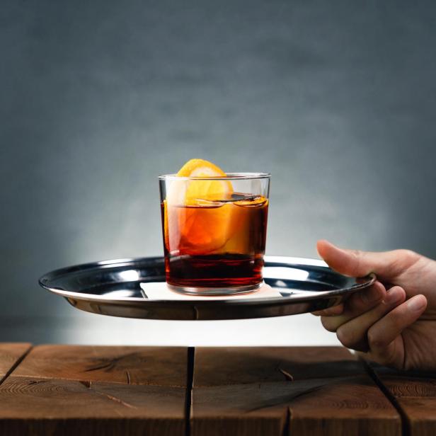 Ein Negroni Sbagliato mit einer Orangenscheibe wird auf einem Tablett serviert.