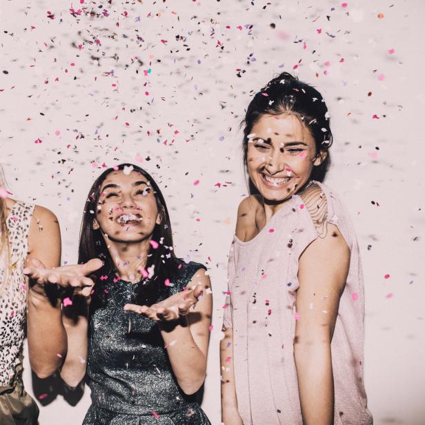 Drei junge Frauen feiern und werfen Konfetti in die Luft.