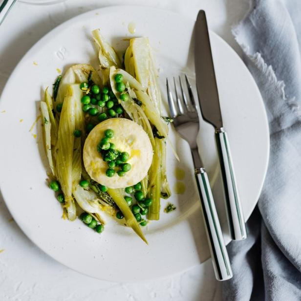 Ein Teller mit Fenchel, Erbsen und einem kleinen Käsekuchen mit Besteck daneben.