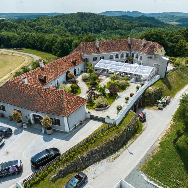 Luftaufnahme eines großen Gutshofs mit roten Dächern, Innenhof und Terrassen-Zelt, umgeben von grünen Hügeln.