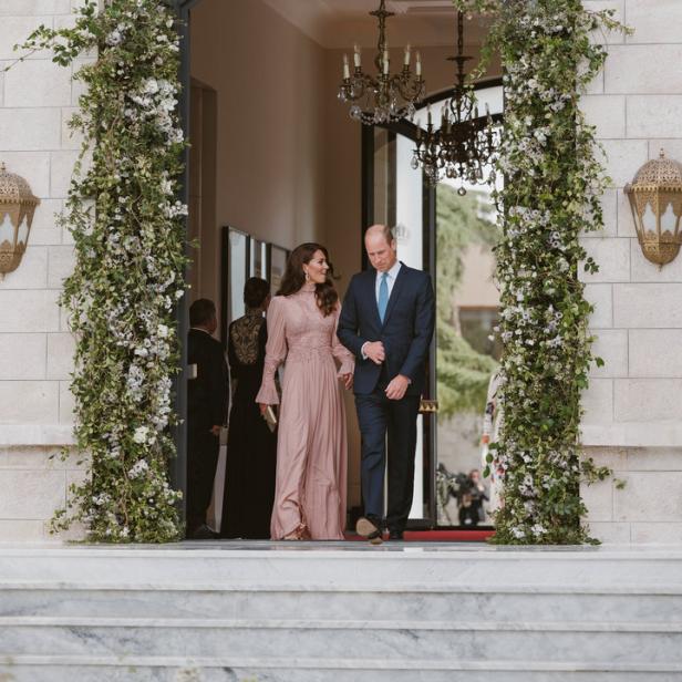 Prinz William und Prinzessin Kate verlassen ein Gebäude, dessen Eingang mit Blumen geschmückt ist.
