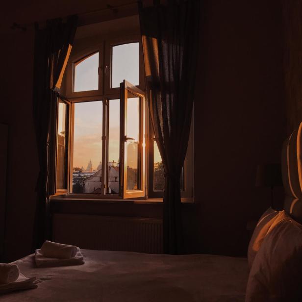 Ein geöffnetes Fenster mit Blick auf eine Stadt im goldenen Abendlicht.