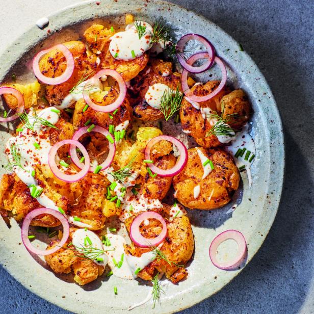 Ein Teller mit zerdrückten Kartoffeln, garniert mit Joghurt, Dill, Schnittlauch und roten Zwiebelringen.