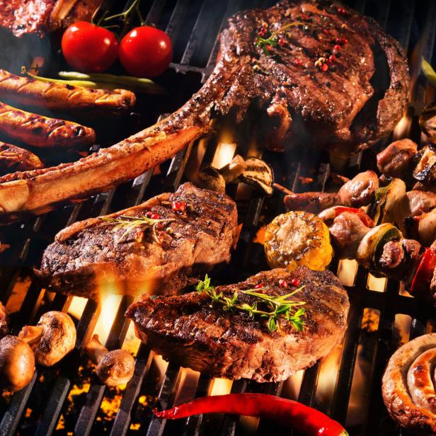 Verschiedene Fleischsorten, Würstchen und Gemüse werden auf einem Grill zubereitet.