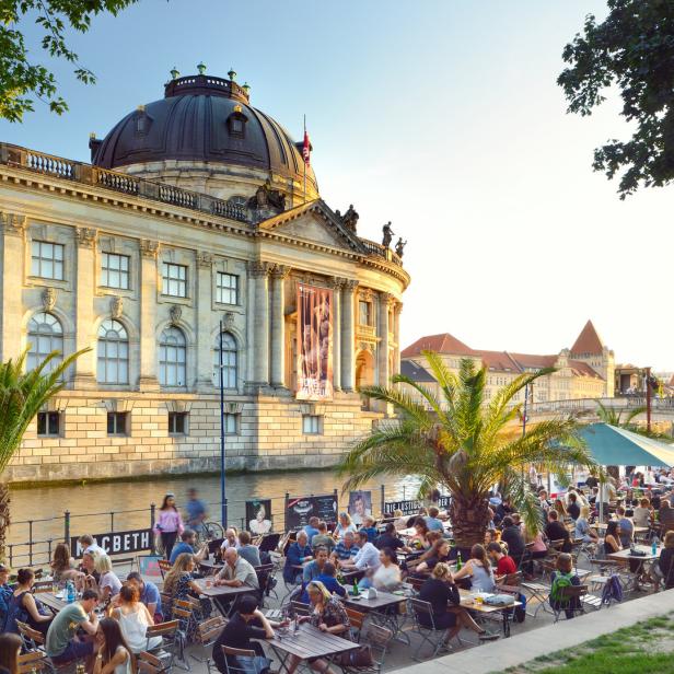 Auf der Museumsinsel in Berlin sitzen Menschen in einem Café am Ufer.