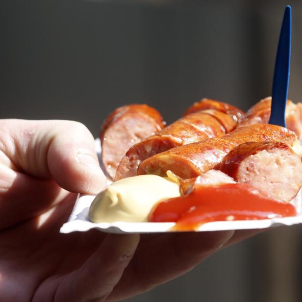 Eine Hand hält eine Schale mit geschnittener Bratwurst, Senf und Ketchup.