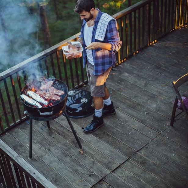 Ein Mann grillt Fleisch und Maiskolben auf einem Balkon.