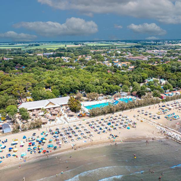 Luftaufnahme eines belebten Strandes mit bunten Sonnenschirmen und einem Schwimmbad im Hintergrund.