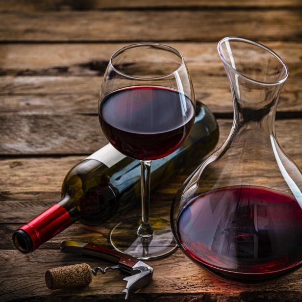 Ein Glas und eine Karaffe Rotwein stehen auf einem Holztisch.