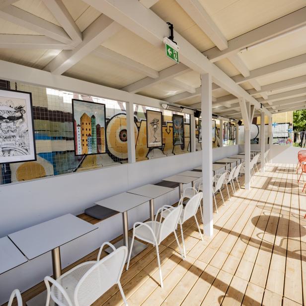 Ein Außenbereich eines Cafés mit Tischen, Stühlen und Kunstwerken an der Wand.