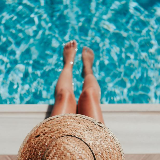 Eine Frau entspannt mit einem Strohhut am Pool.