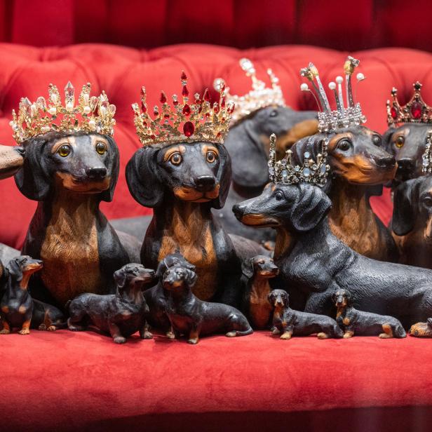 Mehrere Dackel-Figuren mit Kronen sitzen auf einem roten Sofa.