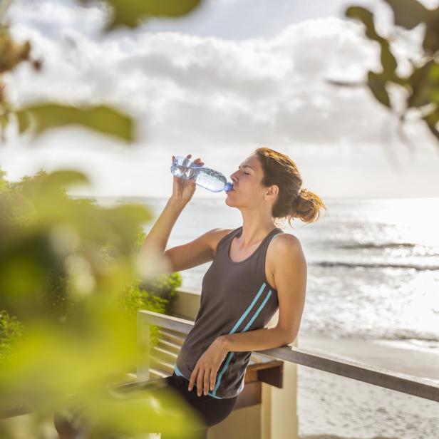 Eine Frau trinkt Wasser vor dem Hintergrund eines Strandes.