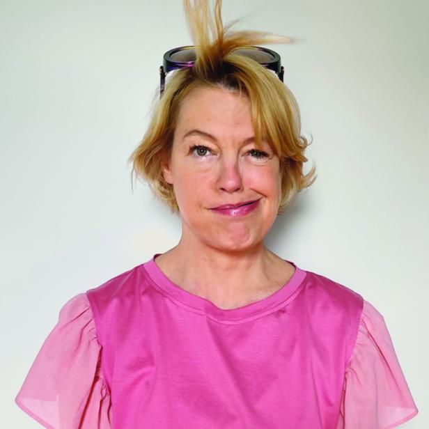 Eine Frau mit blonden Haaren und Sonnenbrille auf dem Kopf zwinkert in die Kamera.