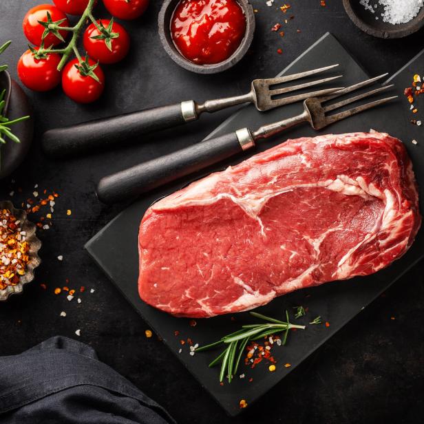 Ein rohes Ribeye-Steak liegt auf einem schwarzen Schneidebrett.