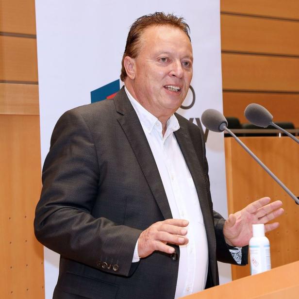 Ein Mann in einem Anzug spricht an einem Rednerpult mit Mikrofonen.