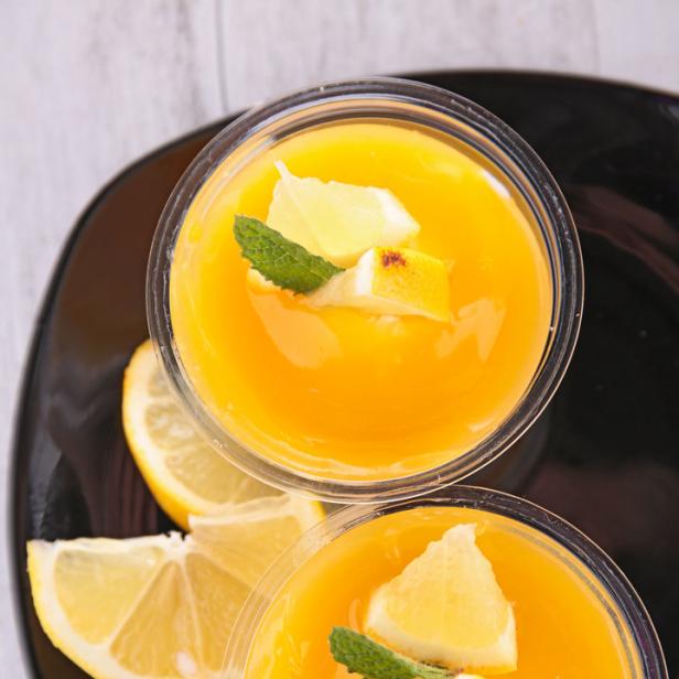 Zwei Gläser mit gelbem Dessert, garniert mit Zitrone und Minze.