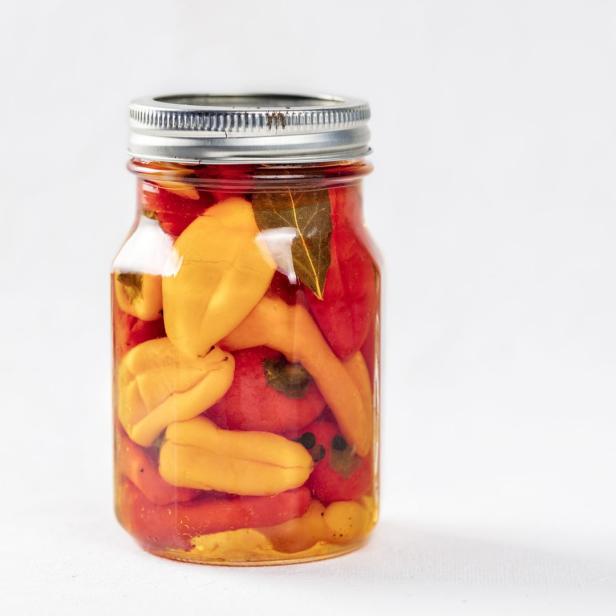 Einmachglas mit eingelegten gelben und roten Paprika auf weißem Grund.
