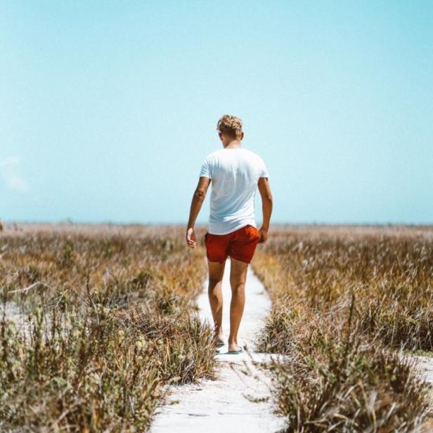 Ein Mann in Shorts geht einen sandigen Pfad entlang durch eine Graslandschaft.