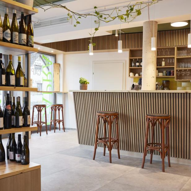 Innenansicht einer Weinbar mit Regalen voller Flaschen und Barhockern.