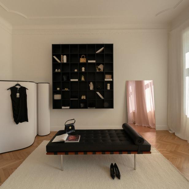 Ein Zimmer mit einem schwarzen Sofa, einem Regal und einem Kleid an einem Raumteiler.