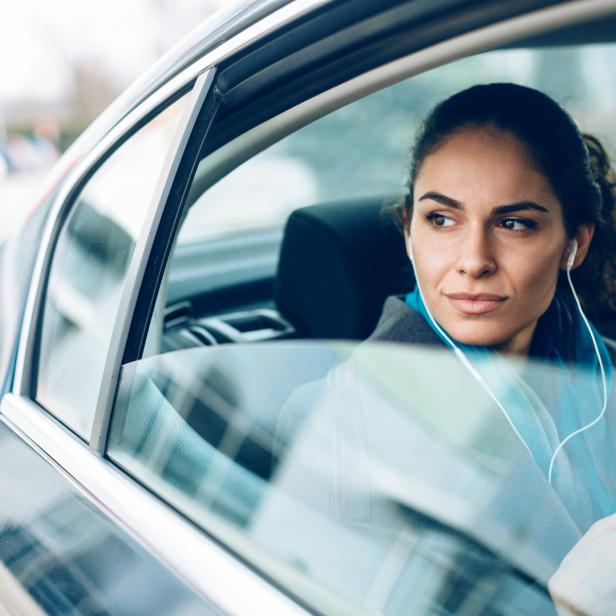 Eine Frau sitzt mit Kopfhörern im Auto und schaut aus dem Fenster.