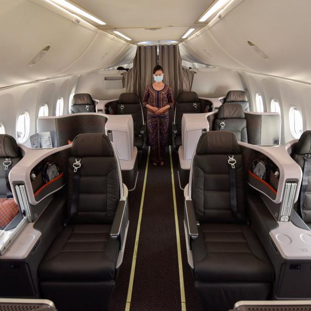 Eine Stewardess mit Maske steht in der Business Class eines Flugzeugs.