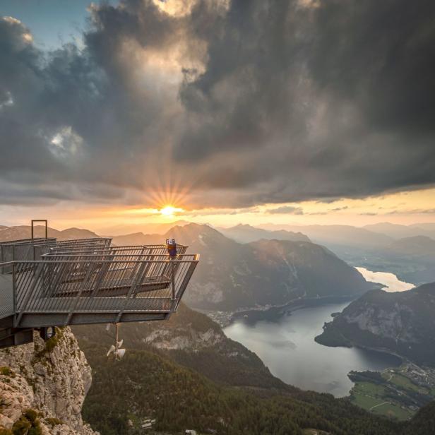 Eine Aussichtsplattform auf einem Berg mit Blick auf einen See bei Sonnenuntergang.