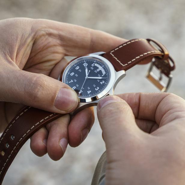 Eine Person hält eine Armbanduhr mit braunem Lederarmband in den Händen.