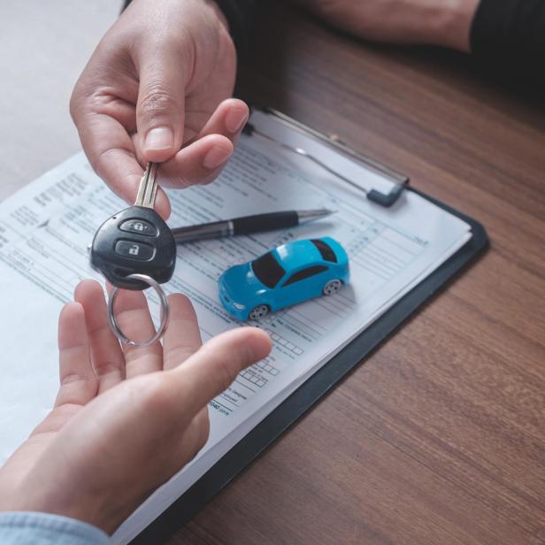 Eine Hand übergibt einen Autoschlüssel über einem Vertrag und einem Spielzeugauto.