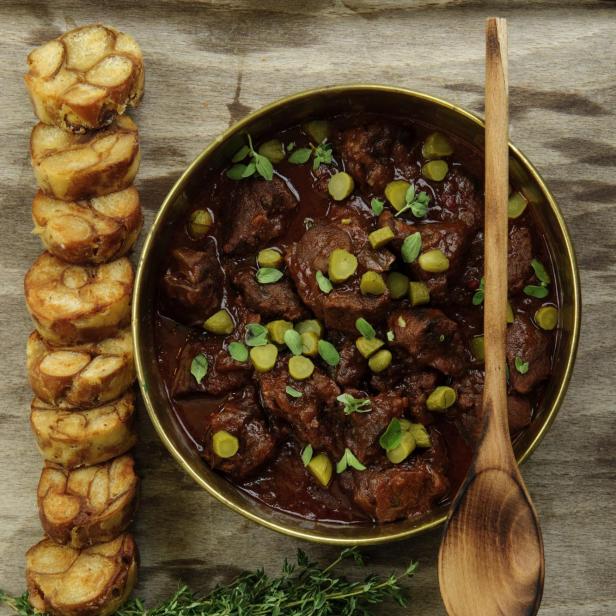 Rindsgulasch mit Gurken und Semmelknödel auf einem Holztisch.
