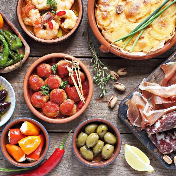 Verschiedene Tapas, darunter Oliven, Fleischbällchen, Käse und Kartoffelgratin, sind auf einem Holztisch angerichtet.