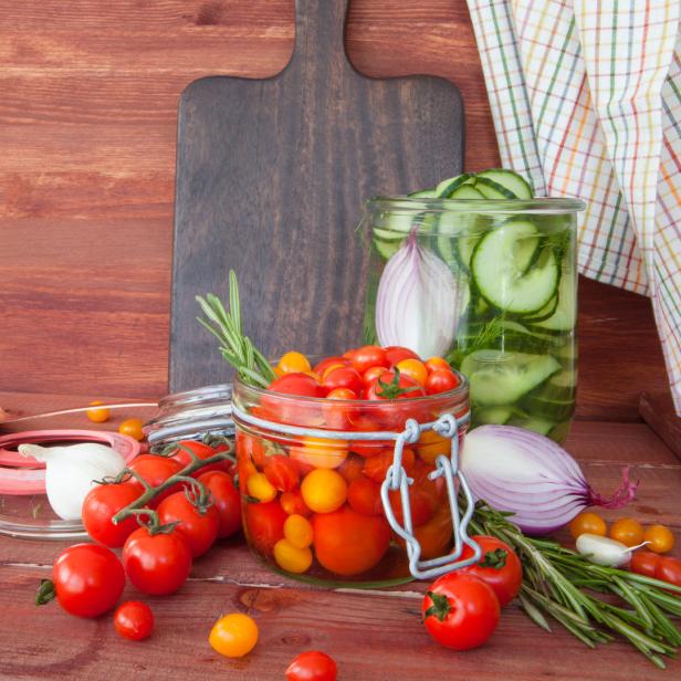 Eingemachte Tomaten und Gurken in Gläsern auf einem Holztisch.
