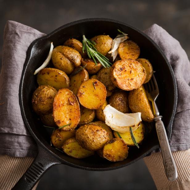 Eine Person hält eine gusseiserne Pfanne mit Bratkartoffeln, Zwiebeln und Rosmarin.