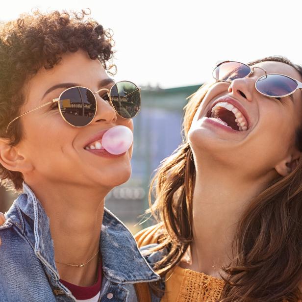 Zwei junge Frauen lachen und eine von ihnen macht eine Kaugummiblase.