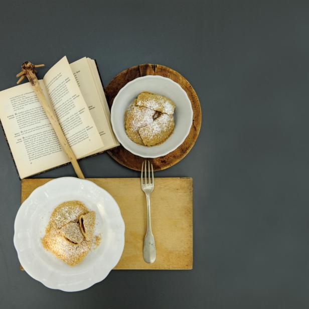 Zwei Teller mit Powidltascherl und ein aufgeschlagenes Kochbuch.
