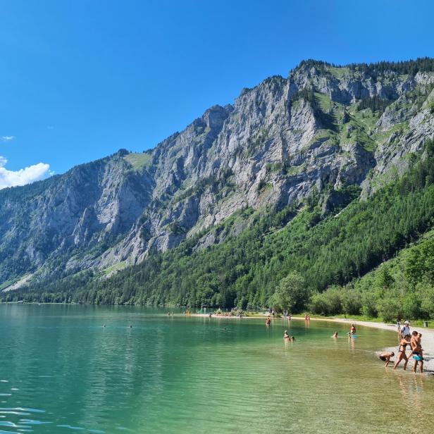 Der smaragdgrüne Traunsee mit Badegästen vor einer steilen Felswand.
