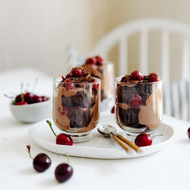 Drei Gläser mit Schokoladenpudding, Kirschen und Schokoladenkuchen stehen auf einem Tisch.
