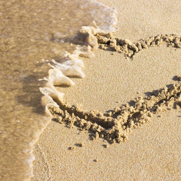 Eine Welle umspült ein in den Sand gezeichnetes Herz.