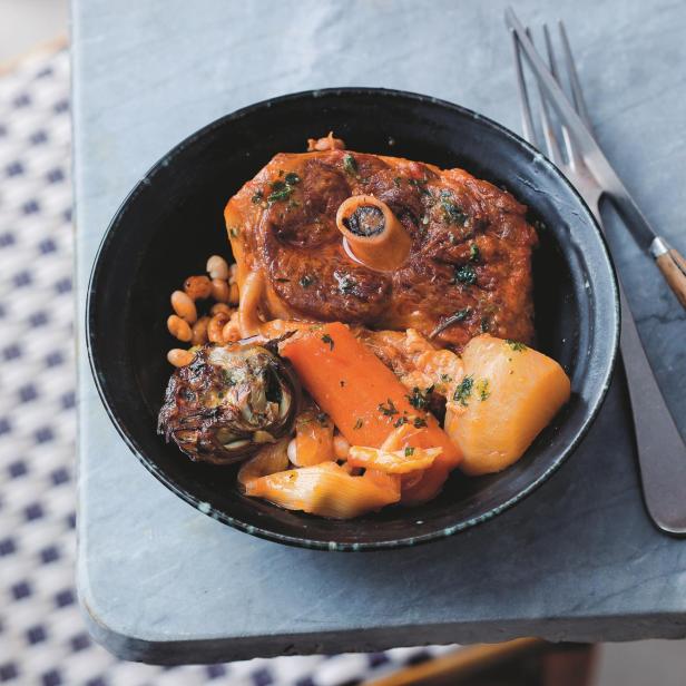 Ossobuco mit Gemüse und weißen Bohnen in einer schwarzen Schüssel.
