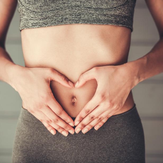 Eine Frau formt mit ihren Händen ein Herz auf ihrem Bauch.
